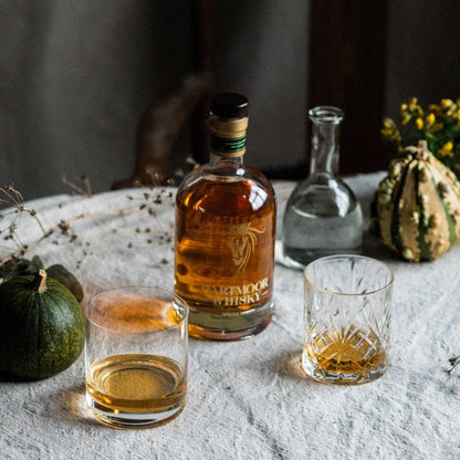 Single malt whisky bottle with amber liquid, plus two short tumblers on a table.