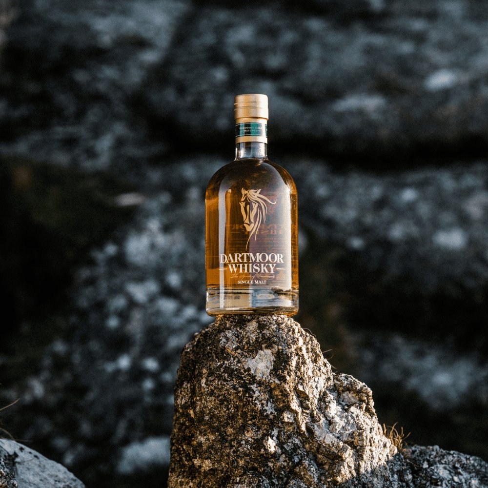 Single malt whisky bottle with amber liquid perched on a rock against a dark background.