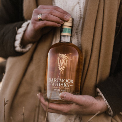 Single malt whisky bottle held in hands, gold cap and front label facing forward.