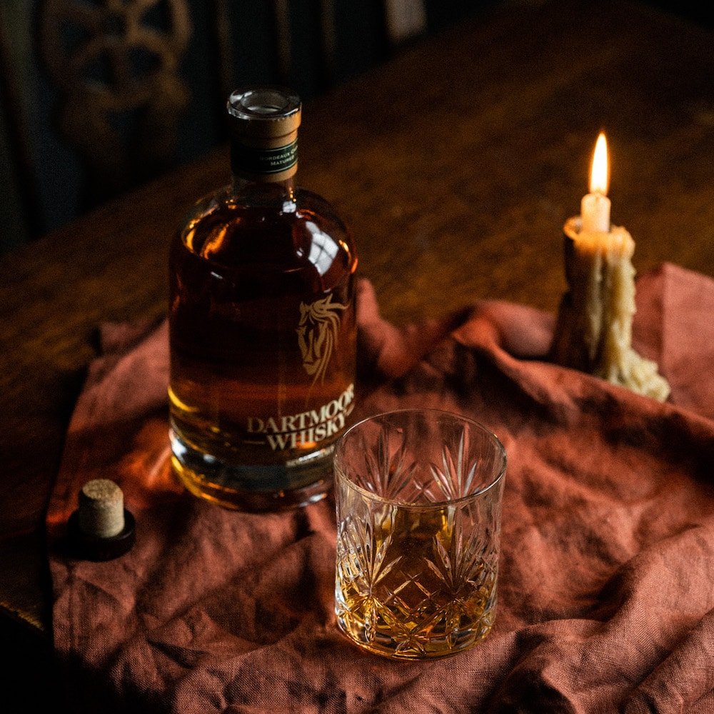 Single malt whisky bottle on a table with an engraved tumbler and a nearby candle.
