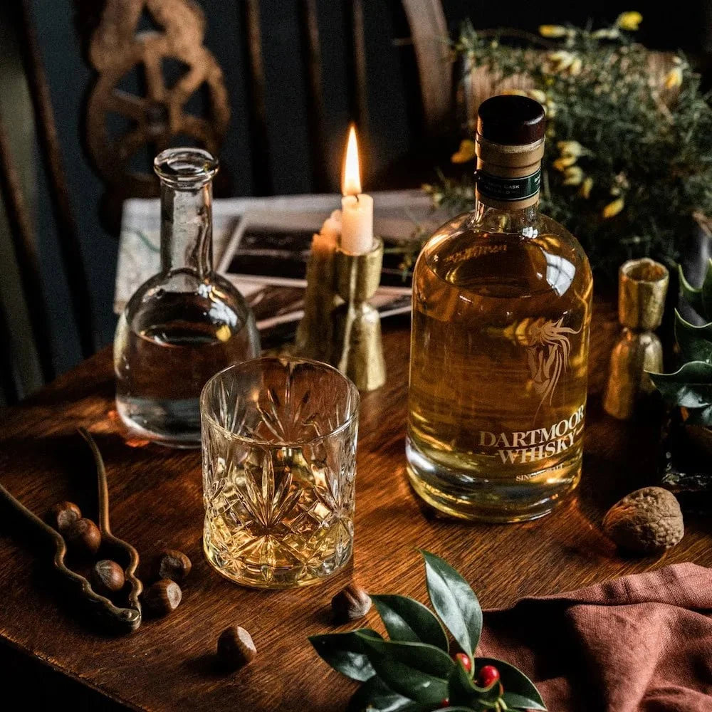 Whisky bottles on a wooden table with lit candle and crystal glasses