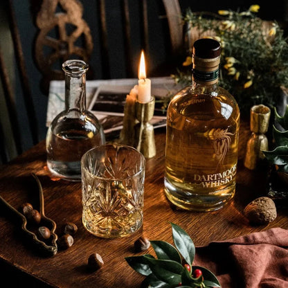 Whisky bottles on a wooden table with lit candle and crystal glasses