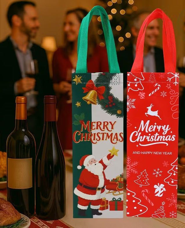 Two Christmas-themed fabric wine bags standing upright on a table, with blurred people and a Christmas tree in the background. One bag is green and white with Santa and 'Merry Christmas' text, and the other is red and white with holiday illustrations and 'Merry Christmas and Happy New Year' text.
