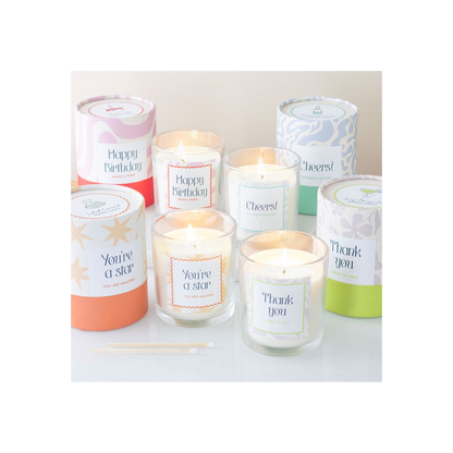 Assorted birthday candles in glass jars, each with different colored labels and lit wicks