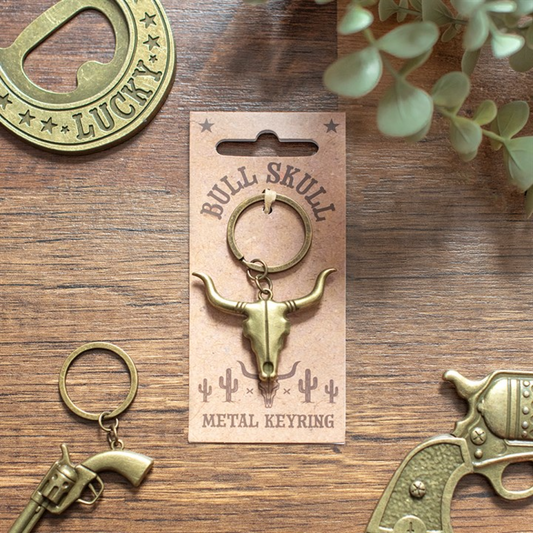 Gold-tone metal bull keyring with ring and horned skull pendant on card