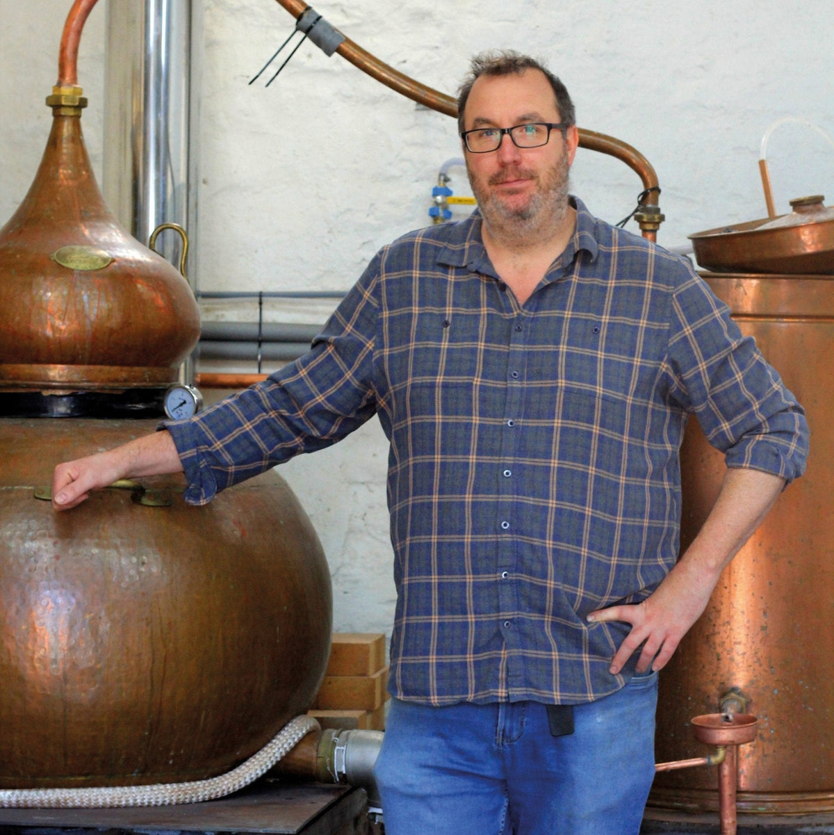 Copper pot still and large copper vessels with pipes in a distillery room