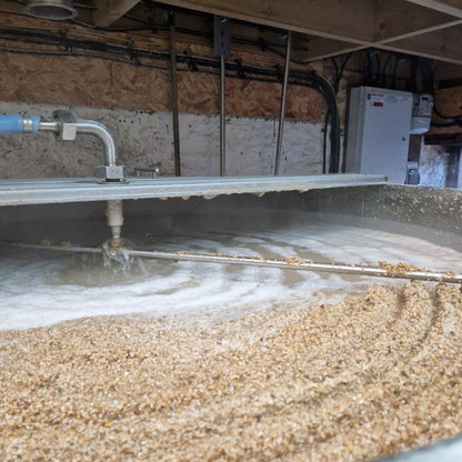 Large vat of rum mash with water flowing from pipes