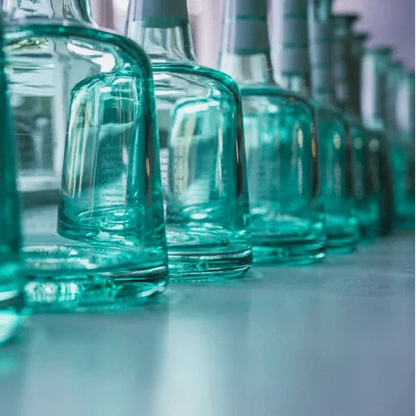 Row of teal glass Island gin bottles with cork tops on a light countertop