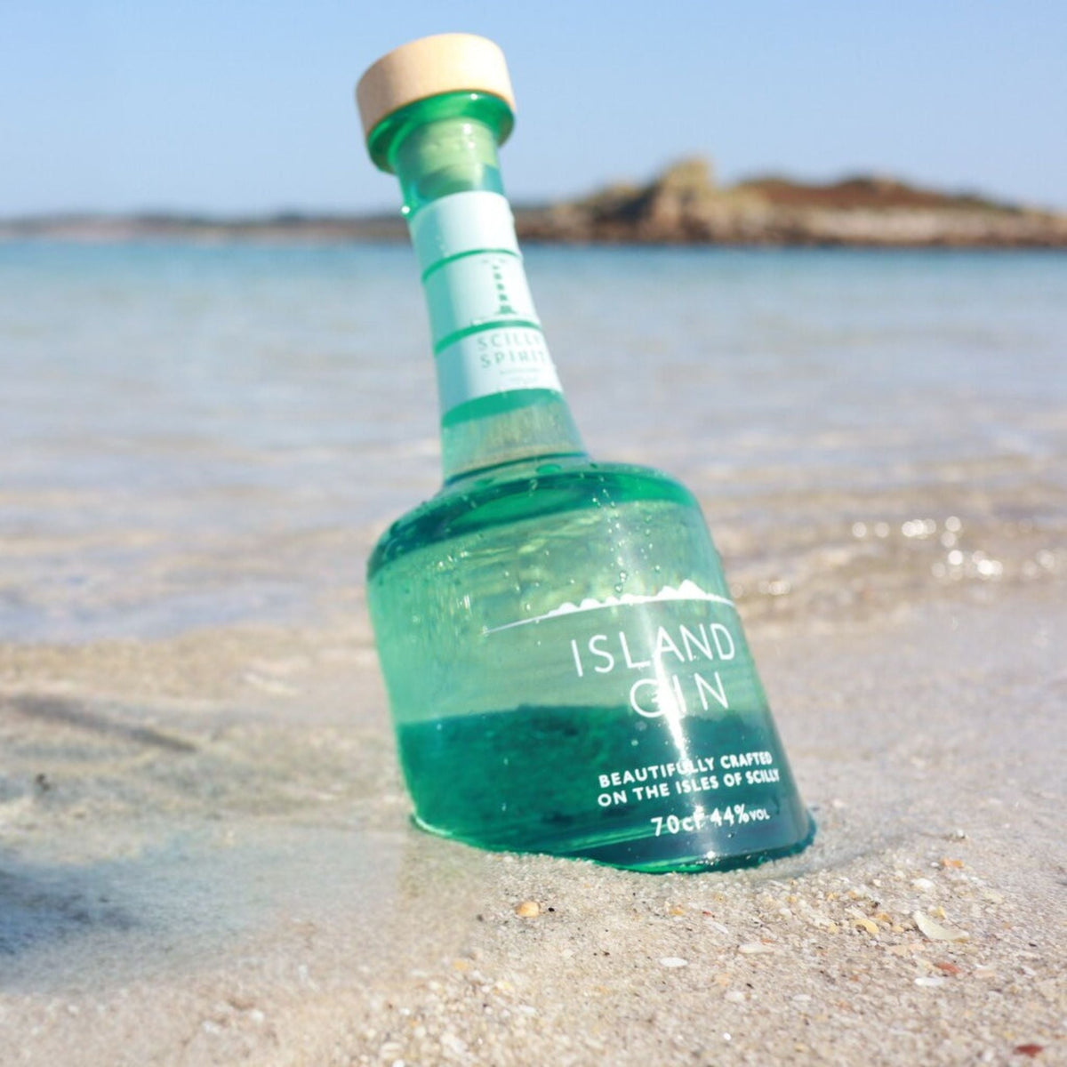 Island gin bottle with teal glass, cork top, and front label on beach sand
